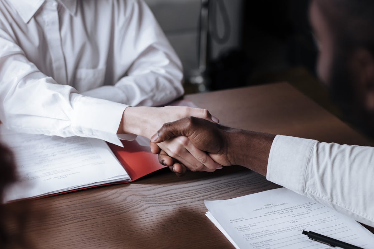 A business handshake over a desk with financial documents